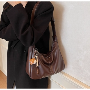 Gros plan du sac hobo en cuir marron avec surpiqûres et pendentif de baseball