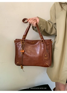 Detail of vintage brown leather tote bag featuring golden hardware and woven charm