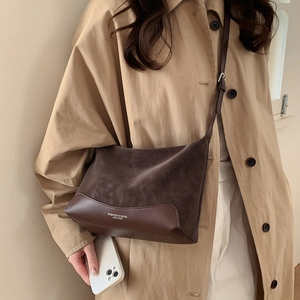 Close-up of dark brown suede shoulder bag with leather splicing and fashion typography