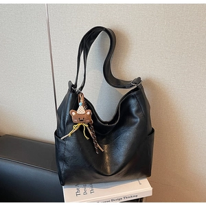 Detail of black glossy leather hobo bag with a cute plush bear charm on white books