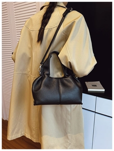 Détail d'un sac à main noir en cuir grainé sur un trench-coat beige pour un look de bureau