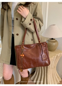 Detail of a brown oil-wax leather tote bag with brand logo and orange beaded tassel