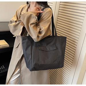 Detail of grey checkered tote bag featuring a front flap pocket and sturdy shoulder straps