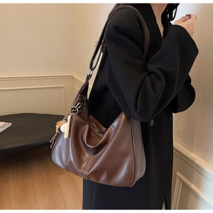 Detail of a brown leather hobo bag featuring contrast stitching and a unique charm
