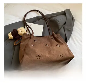 Detail of dark brown suede tote bag featuring laser-cut floral patterns and a plush bear charm