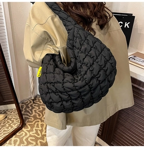 Détail d'un sac matelassé noir avec étiquette fashion jaune porté à l'épaule par un mannequin