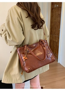 Detail view of brown leather tote bag with wooden bead charm and brand logo embossed