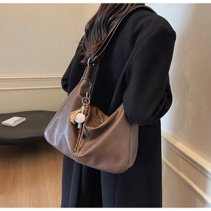Detail view of large brown leather tote bag with baseball charm and textured stitching