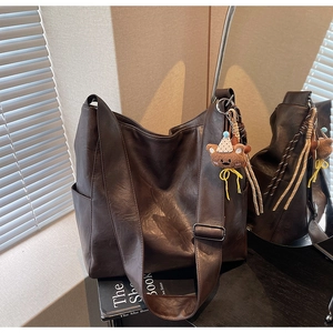 Detail of dark brown hobo shoulder bag featuring a cute bear charm and wide strap