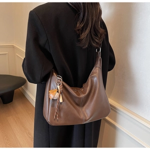 Detail of a brown Hobo tote bag with contrast stitching and creative baseball charm on model