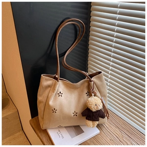 Détail du cabas en daim beige avec découpes florales et breloque ours en peluche