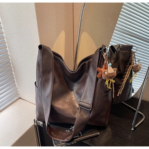 Close-up of dark brown leather tote bag showing wide strap and cute plush bear charm