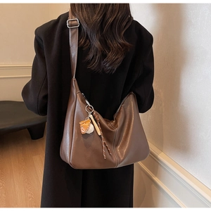 Detail of soft brown leather hobo bag with creative baseball charm and woven rope