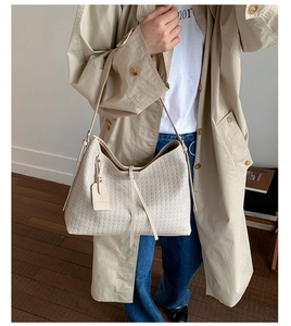 Détail du sac cabas beige tressé avec cordon de serrage et étiquette en cuir sur un modèle