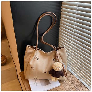 Détail du sac fourre-tout en daim beige avec découpes florales et breloque ours sur bois