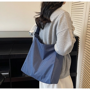 Side view of a large blue checkered canvas tote bag worn by a model in a minimal setting