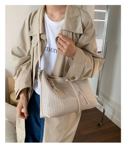 Détail d'un sac cabas en cuir tressé beige porté avec un trench pour un look citadin
