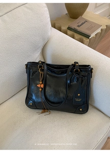 Detail of black glossy leather tote bag with gold stud brand tag on a cream sofa