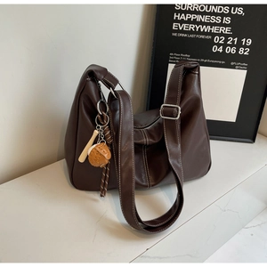 Detail of dark brown tote bag with wide strap and decorative glove keychain charm