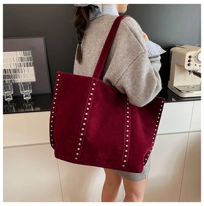 Grand sac cabas en daim bordeaux avec clous argentés porté par un mannequin chic