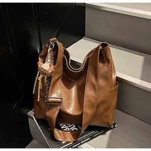Brown vintage leather tote bag with wide strap and cute plush bear charm on a stack of books