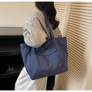 Detail of blue plaid canvas tote bag showing the front pocket and large capacity design