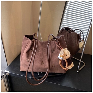 Détail du sac cabas en daim marron avec motifs floraux découpés au laser et breloque ours