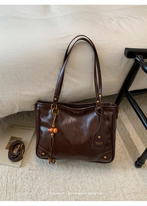 Detail of dark brown leather tote bag with logo embossing and wooden bead tassel ornament