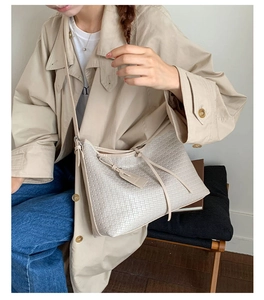 Détail du sac à bandoulière beige tressé avec pompon et étiquette sur un mannequin