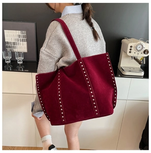 Détail d'un sac cabas bordeaux en daim avec rivets argentés dans un décor minimaliste