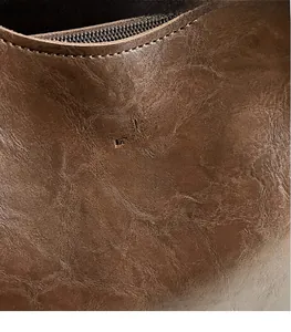 Close-up of leather texture and embossed logo on brown commuter tote shoulder bag