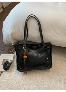 Detail of black leather tote bag with gold hardware and a wooden gourd tassel pendant