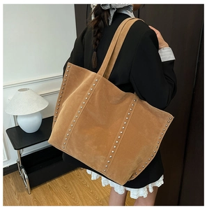 Sac cabas en daim marron à clous argentés porté par un mannequin en intérieur doux