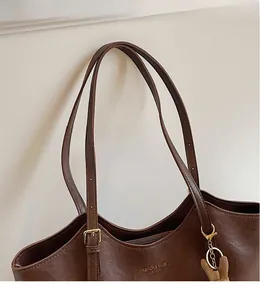 Detail of adjustable shoulder strap with gold buckle and logo on dark brown tote bag