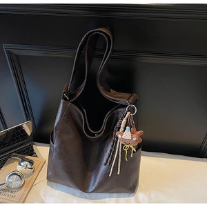 Detail of dark brown leather tote bag with plush bear charm and metallic magnetic buckle