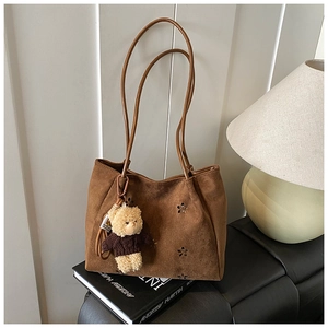 Détail d'un sac cabas en daim marron avec motifs floraux découpés au laser et breloque ours