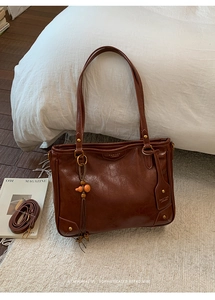 Close-up of brown leather tote bag with retro tassel charm and adjustable shoulder strap