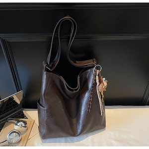 Detail of dark brown leather tote bag with side pocket and cute animal charm on white bed