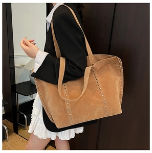 Détail du sac cabas en daim marron avec des rangées verticales de rivets métalliques