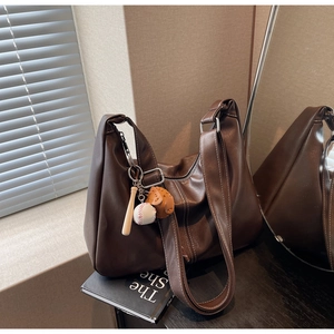 Detail of dark brown leather tote bag featuring contrast stitching and baseball bag charms