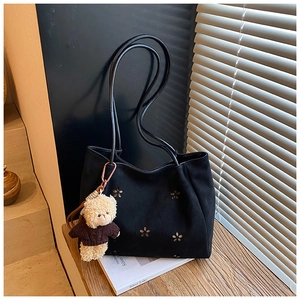 Détail d'un sac cabas noir ajouré à motifs floraux et petit pendentif en forme d'ours