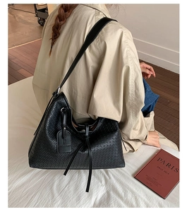 Détail d'un sac cabas noir à texture tressée avec bandoulière et étiquette déco