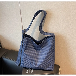 Blue plaid canvas tote bag with adjustable shoulder strap shown on a leather chair