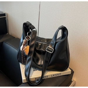 Detail of black leather tote bag with white stitching and decorative glove pendant
