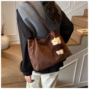Détail du sac en daim marron avec motifs floraux ajourés et pendentif ours en peluche