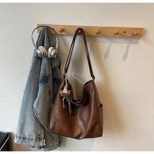 Detail of a brown Hobo shoulder bag with a teddy bear charm hanging on a wooden hook
