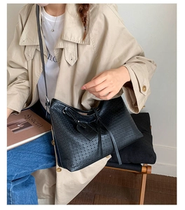 Détail du sac cabas noir à texture tressée porté à l'épaule avec un trench-coat kaki