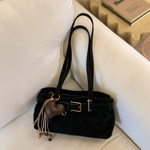 Detail of vintage black suede handbag with heart charm and tassels on a white sofa