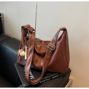 Detail of a brown leather hobo bag with baseball charm on a black magazine background