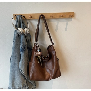 Retro brown oversized bucket bag with a knit bear charm hanging on a wooden wall hook
